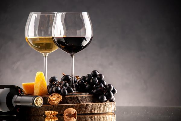 widok z przodu kieliszki do wina swieze winogrona orzechy wloskie zolty ser na desce przewrocona butelka na ciemnym tle